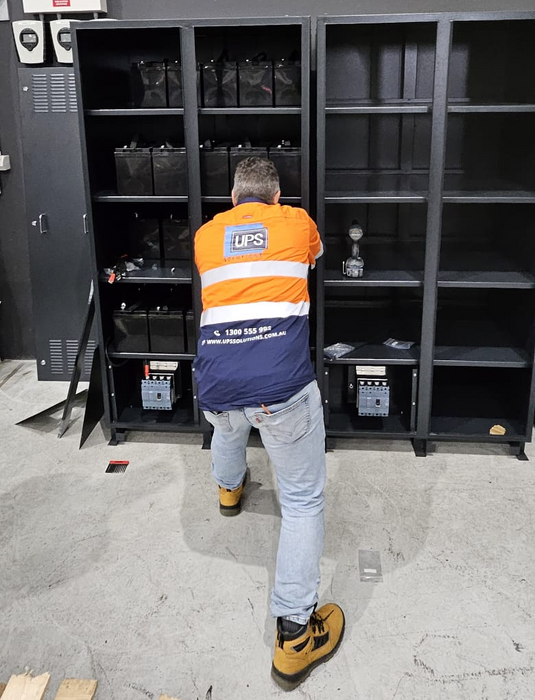 UPS Solutions technician testing and replacing UPS batteries in a battery cabinet